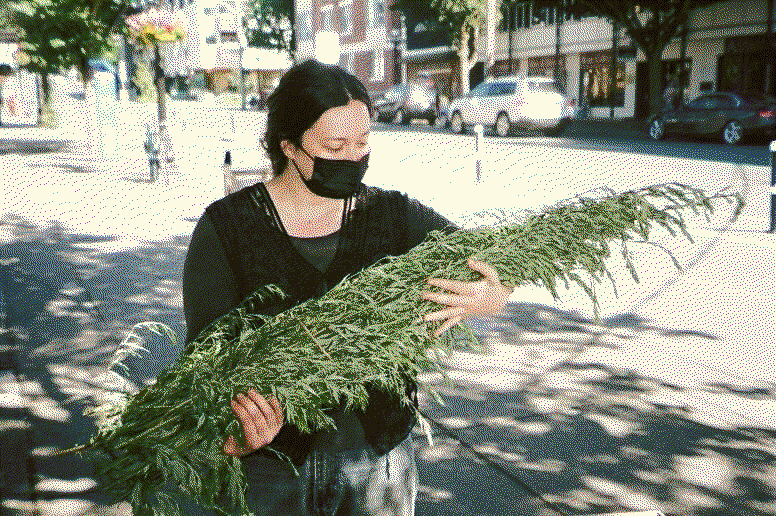 the shop owner, Anna, standing outside carrying a big bundle of greenery